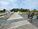 two people in military uniforms and one in civilian attire look at a truck fuel facility