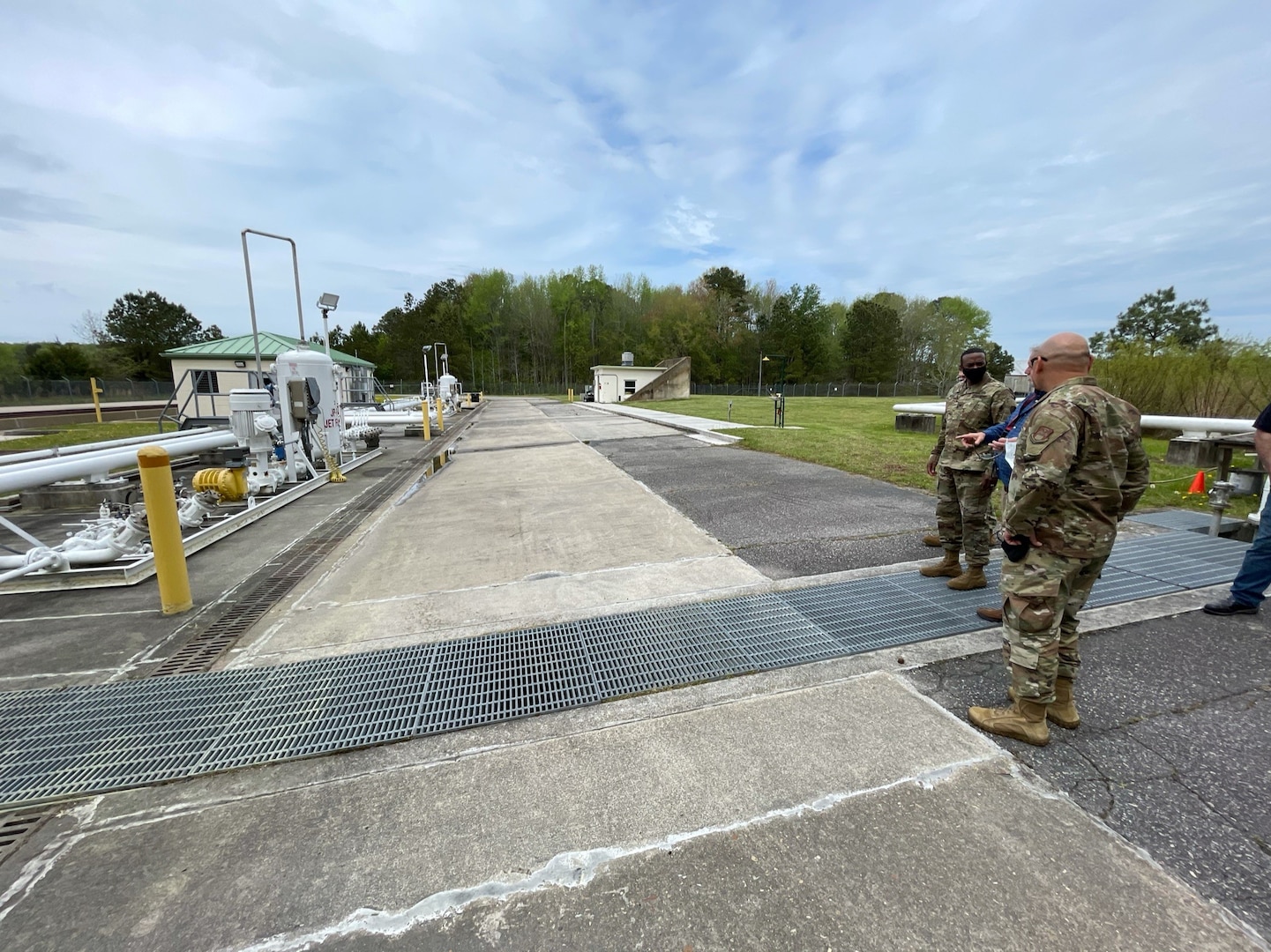 two people in military uniforms and one in civilian attire look at a truck fuel facility