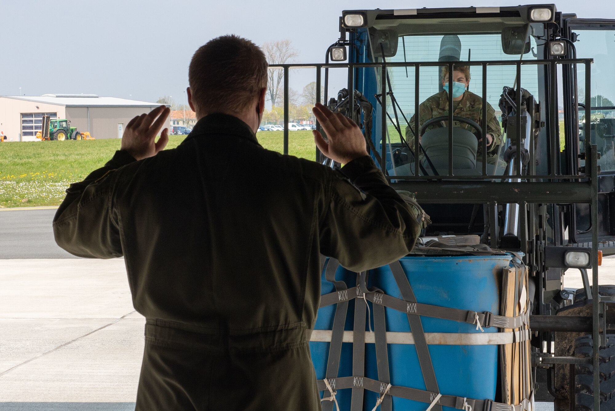 An Airman guides a forklift driver toward an aircraft.