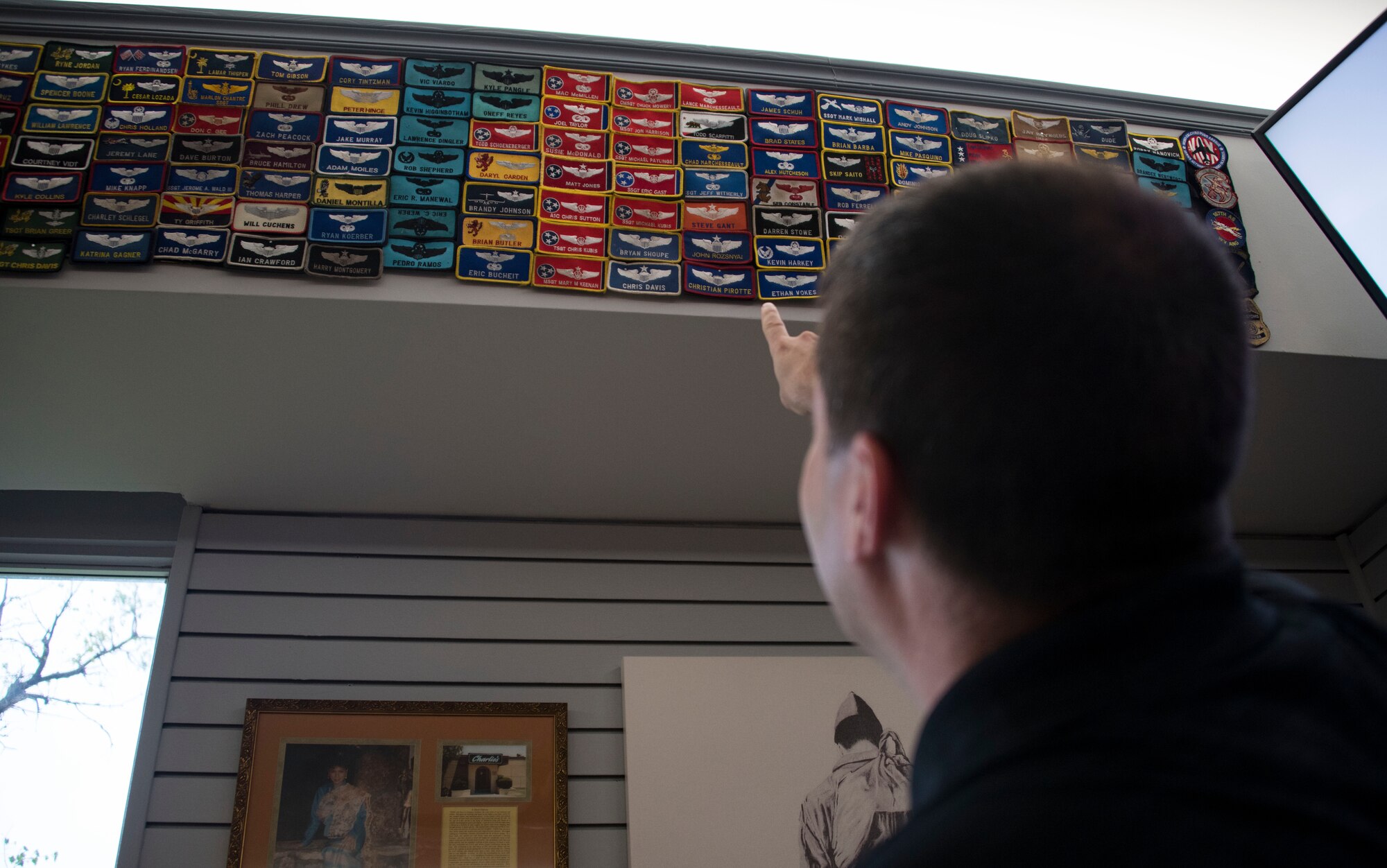 A Charlie’s Lounge patron points to his patch on display inside of the lounge April 15, 2021, at Altus Air Force Base, Oklahoma. It has been a longstanding tradition for Charlie to collect and showcase patches from Airmen. (U.S. Air Force photo by Airman 1st Class Amanda Lovelace)