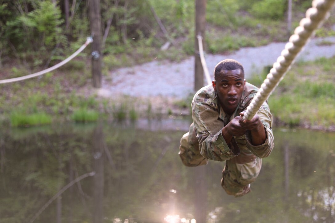 A soldiers crawls on a rope over a body of water.