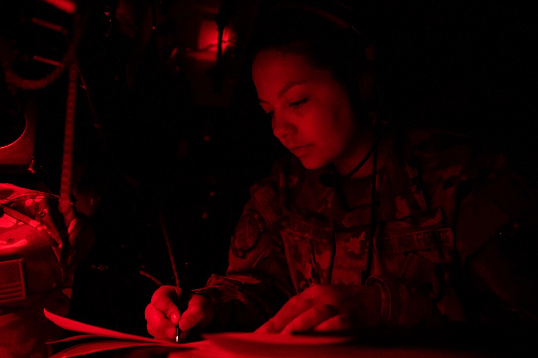An airman illuminated by red light sits at desk writing on a piece paper.
