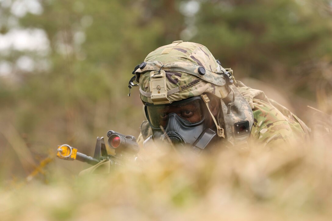 A soldier wearing a gas mask lies on the ground holding a weapon.