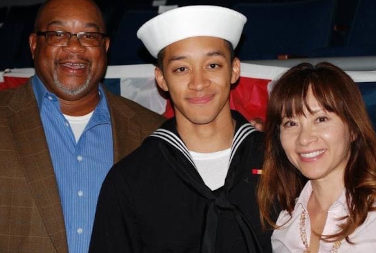 A young man in a military uniform stands between his parents and smiles for a photo.