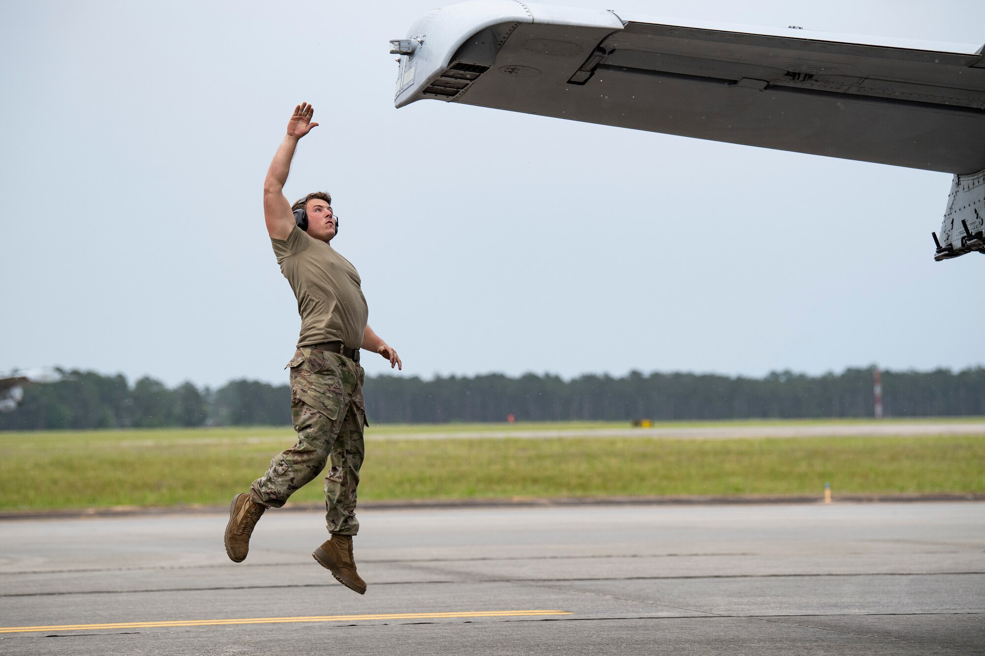 A photo of an Airman jumping to touch the wing tip of an aircraft
