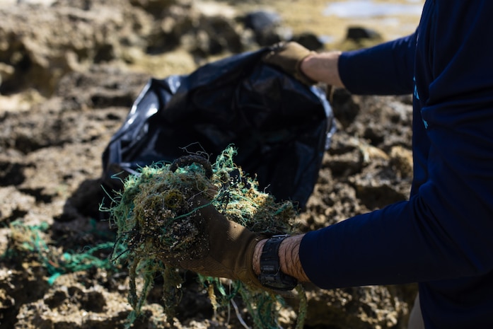 Dane Christiansen, bio-science technician, Environmental Protection and Compliance Division, Marine Corps Base Hawaii, stows a mass of rope and netting in a trash bag on the shore of Fort Hase beach, during the semi-annual base cleanup, MCBH, April 15, 2021. The semi-annual base cleanup occurs every April and October, with the goal of clearing manmade debris from the natural environment. (U.S. Marine Corps photo by Lance Cpl. Brandon Aultman)