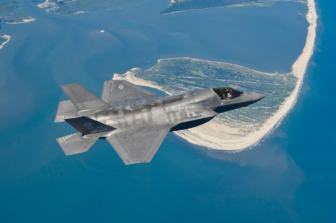 A military aircraft flies over water.