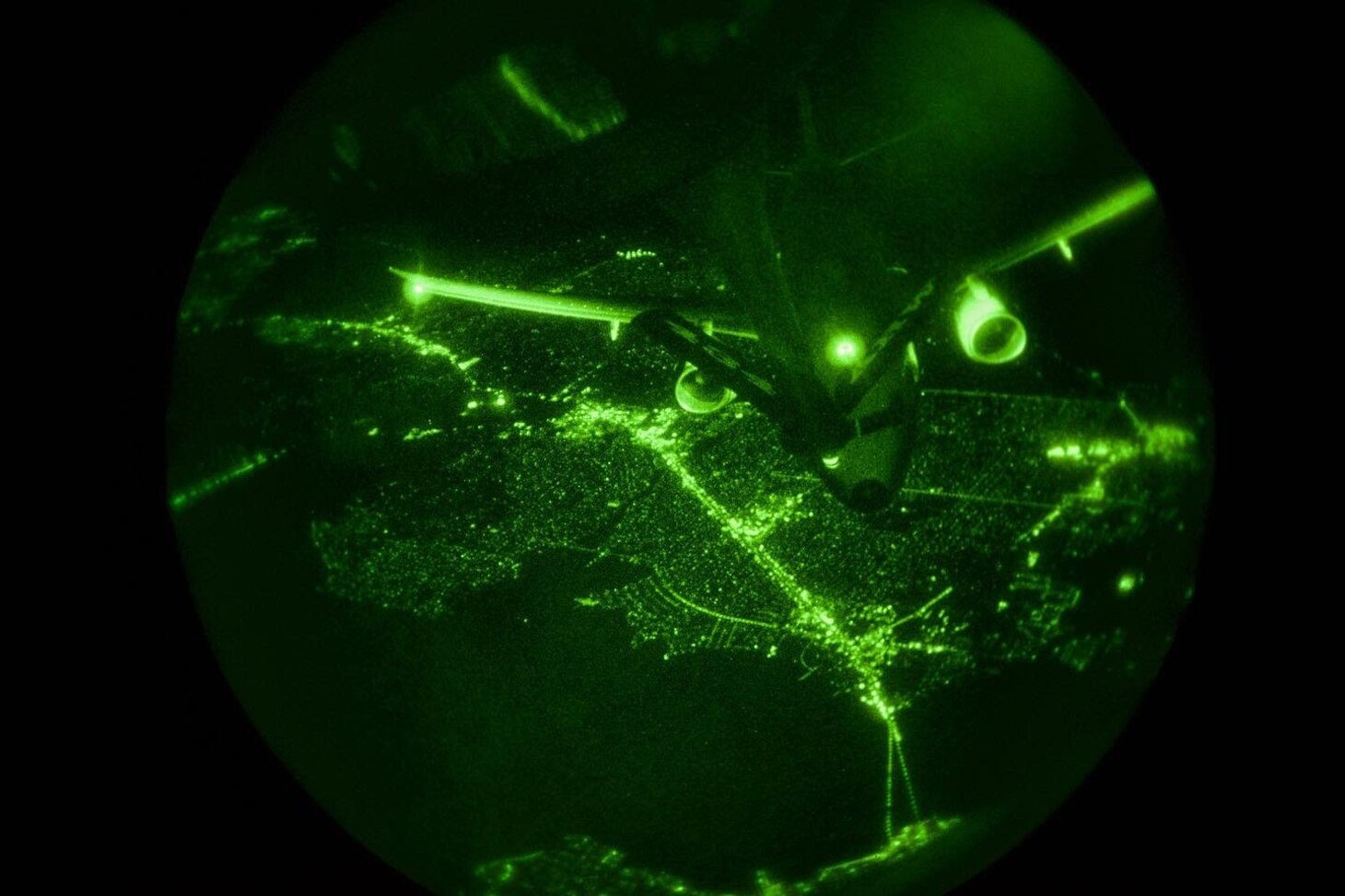 Seen on a night vision scope, a military aircraft approaches the refueling boom of another aircraft.