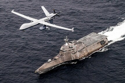 An unmanned aircraft flies over a Navy ship traveling in the sea.