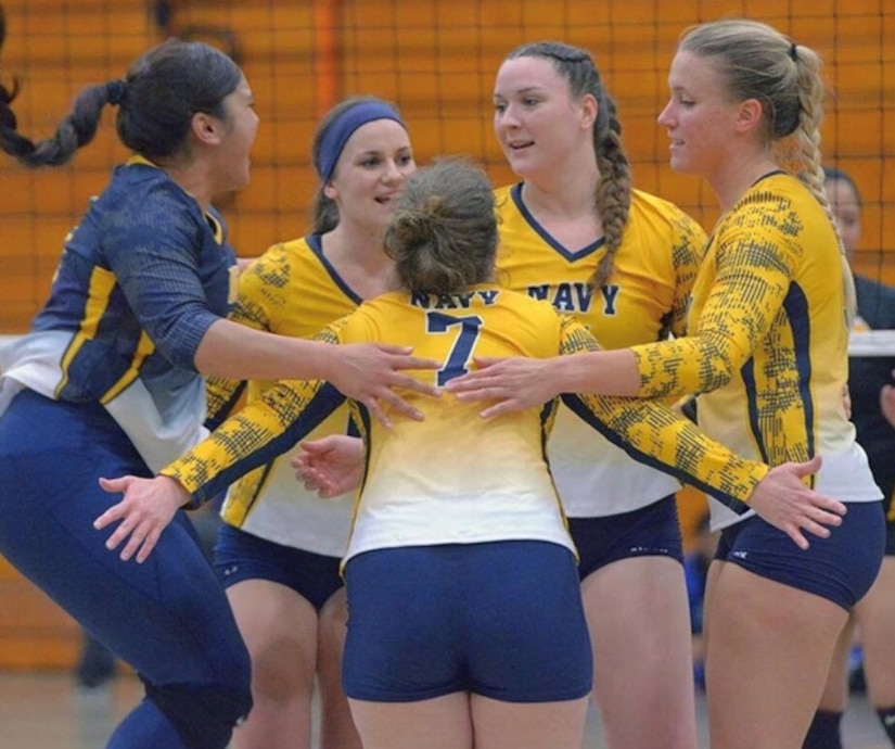 Five members of the All-Navy women's volleyball team huddle on the court during a match.