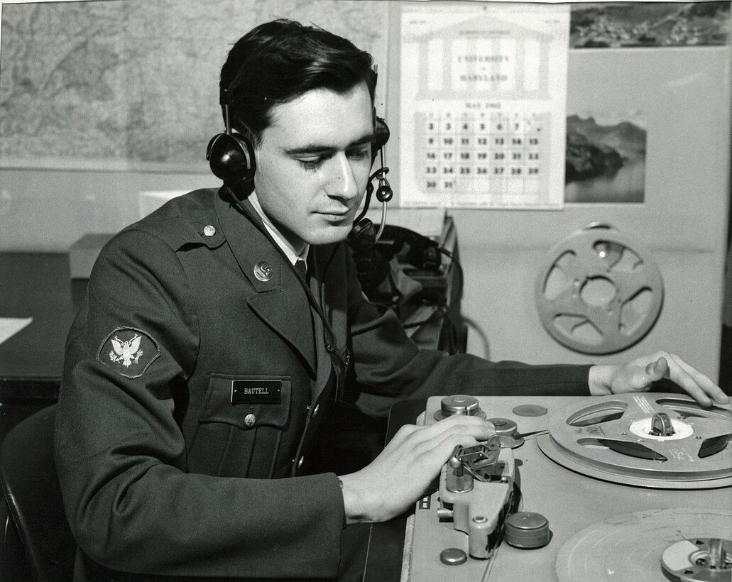 A uniformed man in headphones touches DJ equipment in a radio studio.