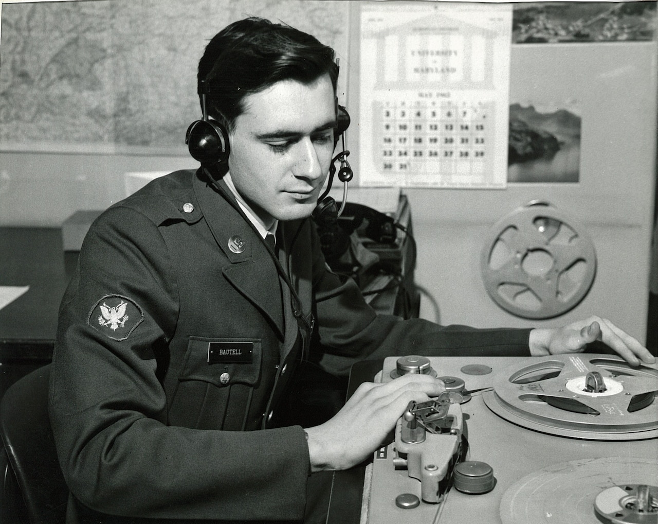 A uniformed man in headphones touches DJ equipment in a radio studio.