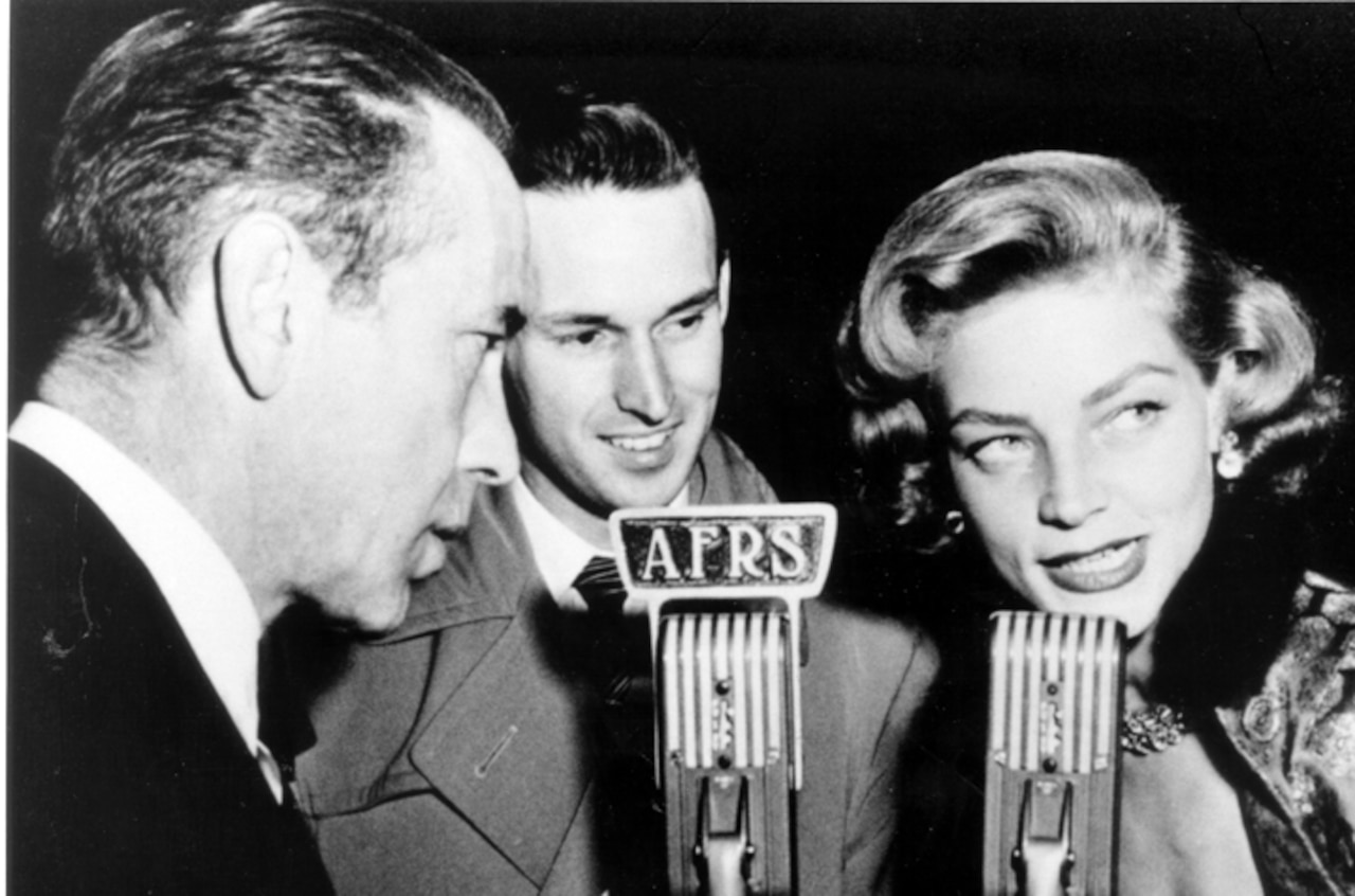 A woman and two men stand in front of a 40s-era microphone that says "AFRS."
