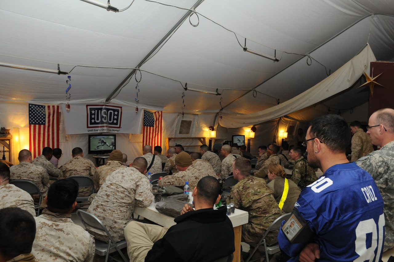 Several seated people surround a small TV in a tent.
