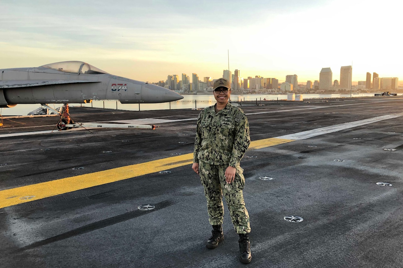 A woman in uniform stands on the deck of an aircraft carrier.