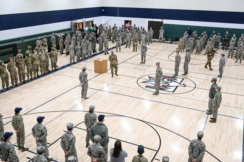 Chief Walker speaks to students standing in formation in a gymnasium.