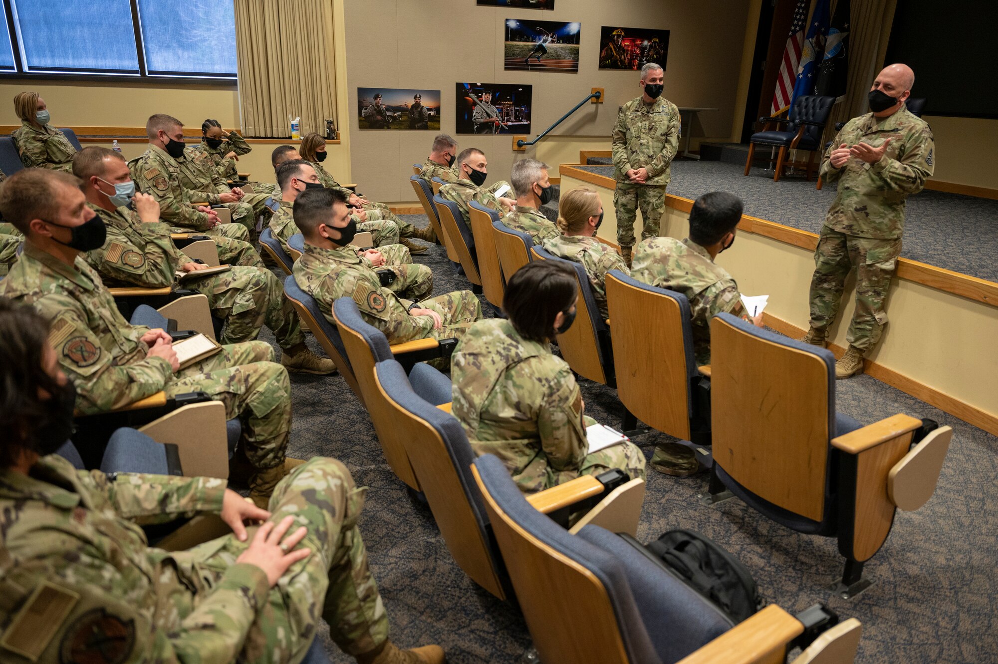 A woman in an audience speaks to a man at the front of an audience.