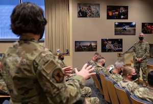 A woman in an audience speaks to a man at the front of an audience.