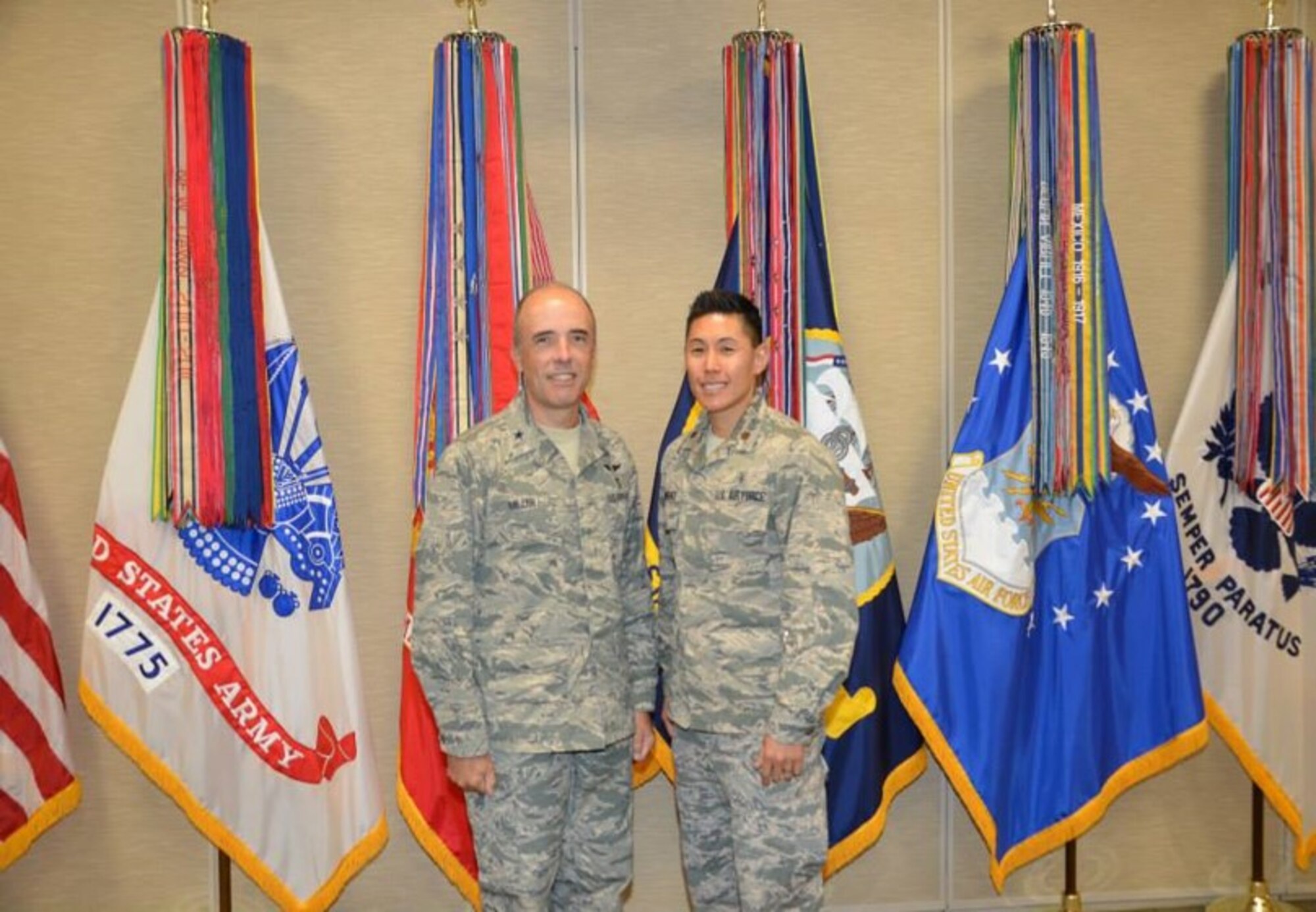 Two men stand in front of flags