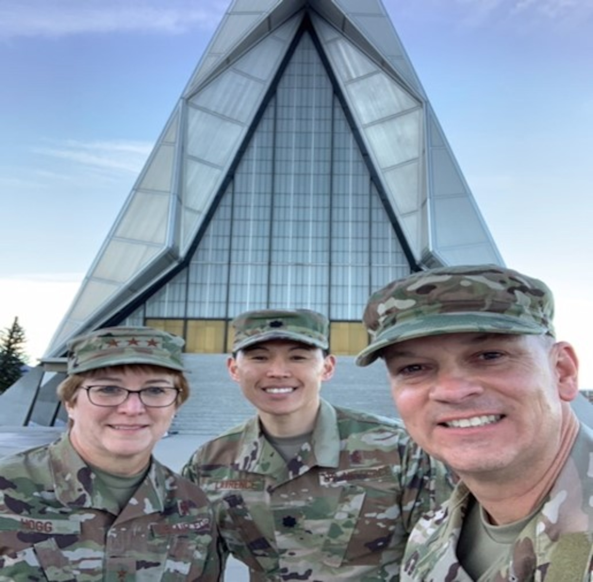 Three individuals stand in front of the Air Force Academy