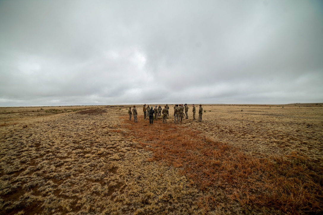 Airman stand in a flat field with low brown vegetation.