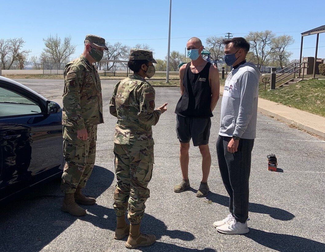 Col. Carroll and Chief Master Sgt. Walker visit with Senior Airman Kevin Alvaran and Senior Airman Craig Sarnak in a parking lot.