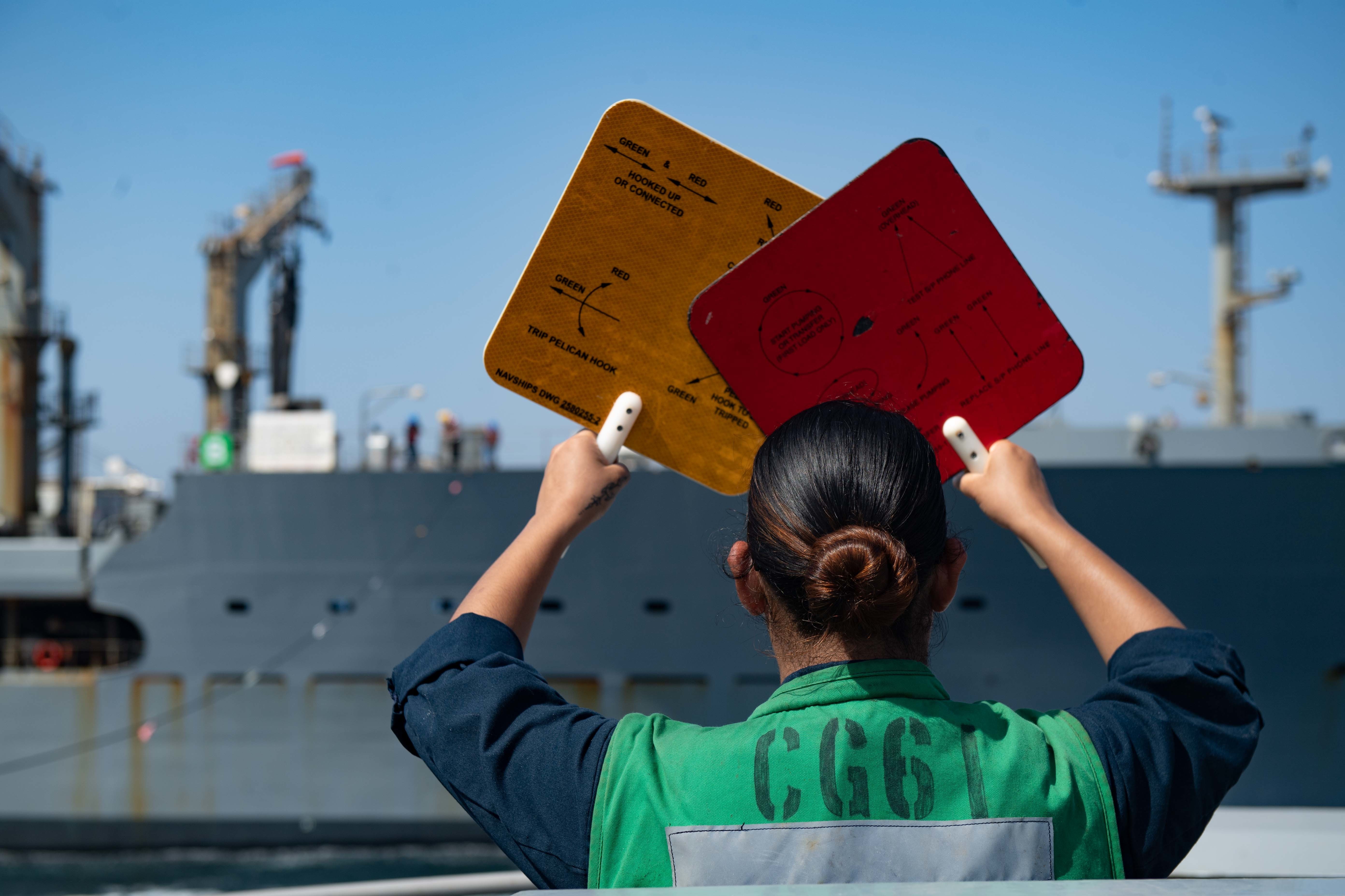 A Sailor uses signal paddles during a replenishment-at-sea between USS Monterey (CG 61) and USNS Patuxent (T-AO 201) in the Arabian Gulf.