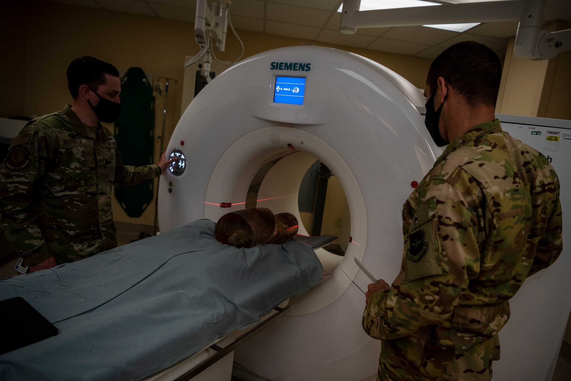 An Airman shows a higher ranking Airman how a large machine scans the body.