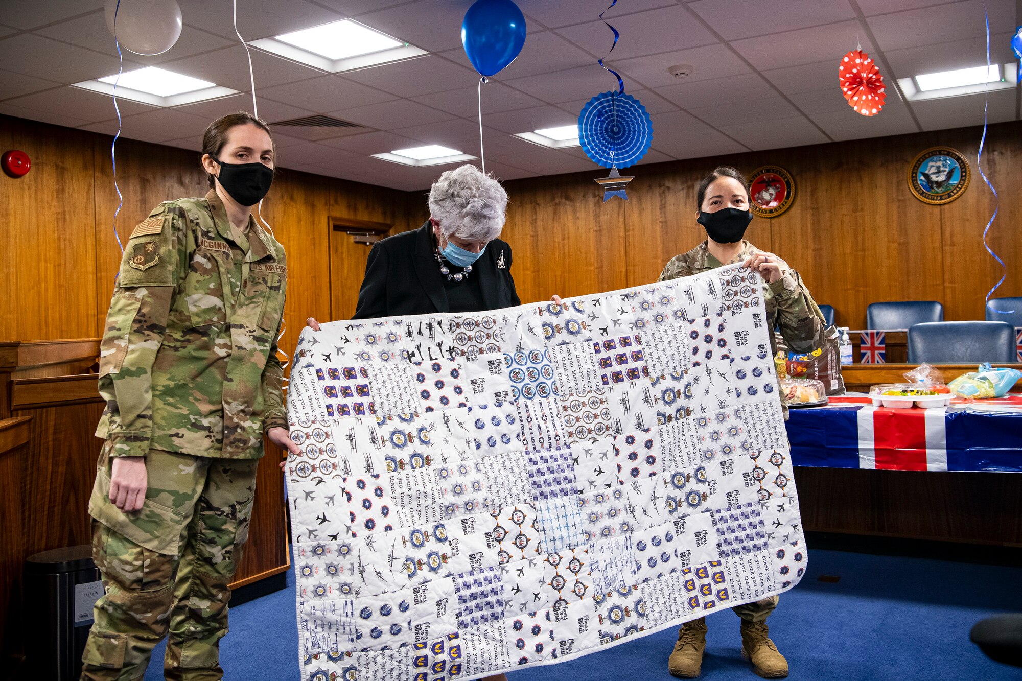 Maj. Danelle McGinnis, left, 501st CSW deputy staff judge advocate, and Master Sgt. Miriam Pantoja, right Judge Advocate Office, NCOIC of general law, present a quilt to Valerie Lucas,  501st Combat Support Wing British liaison officer, during a celebration at RAF Alconbury, England, April 23, 2021. The 501 CSW/JA office celebrated Mrs. Lucas for her 60 years of service as the British liaison officer at RAF Alconbury. (U.S. Air Force photo by Senior Airman Eugene Oliver)