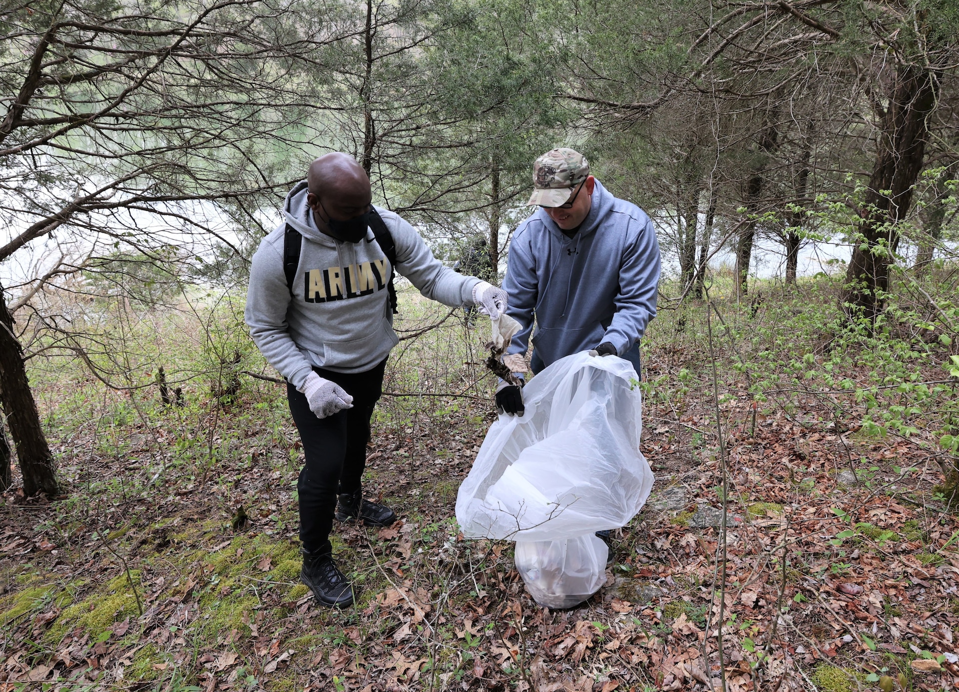 men and women gathering garbage and debris in the woods.