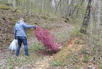 men and women gathering garbage and debris in the woods.