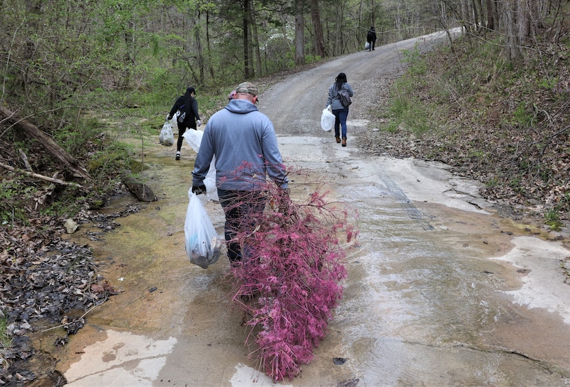 men and women gathering garbage and debris in the woods.