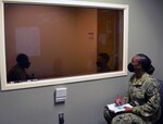 Petty Officer 2nd Class Ebiye Osadare (far right), a Navy instructor for the METC Behavioral Health Technician program, monitors a mock counseling session from behind the glass between BHT students Airman Frederick Hall (left) and Seaman Chery Gonzales-Polanco (right).