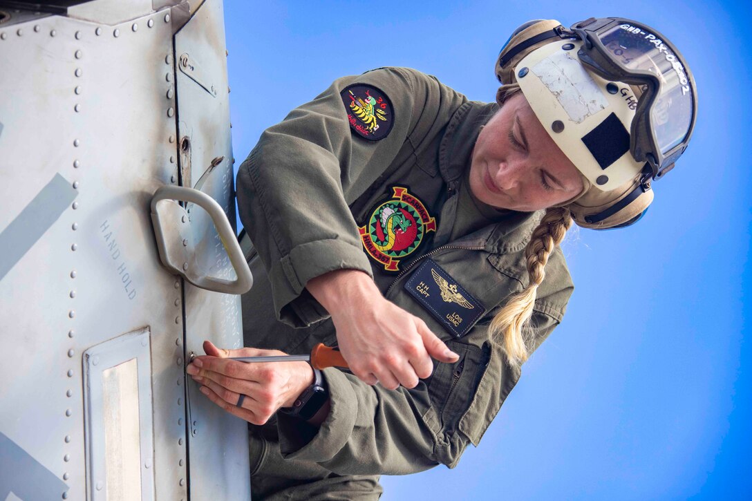 A Marine uses a tool to screw a bolt to a military aircraft.