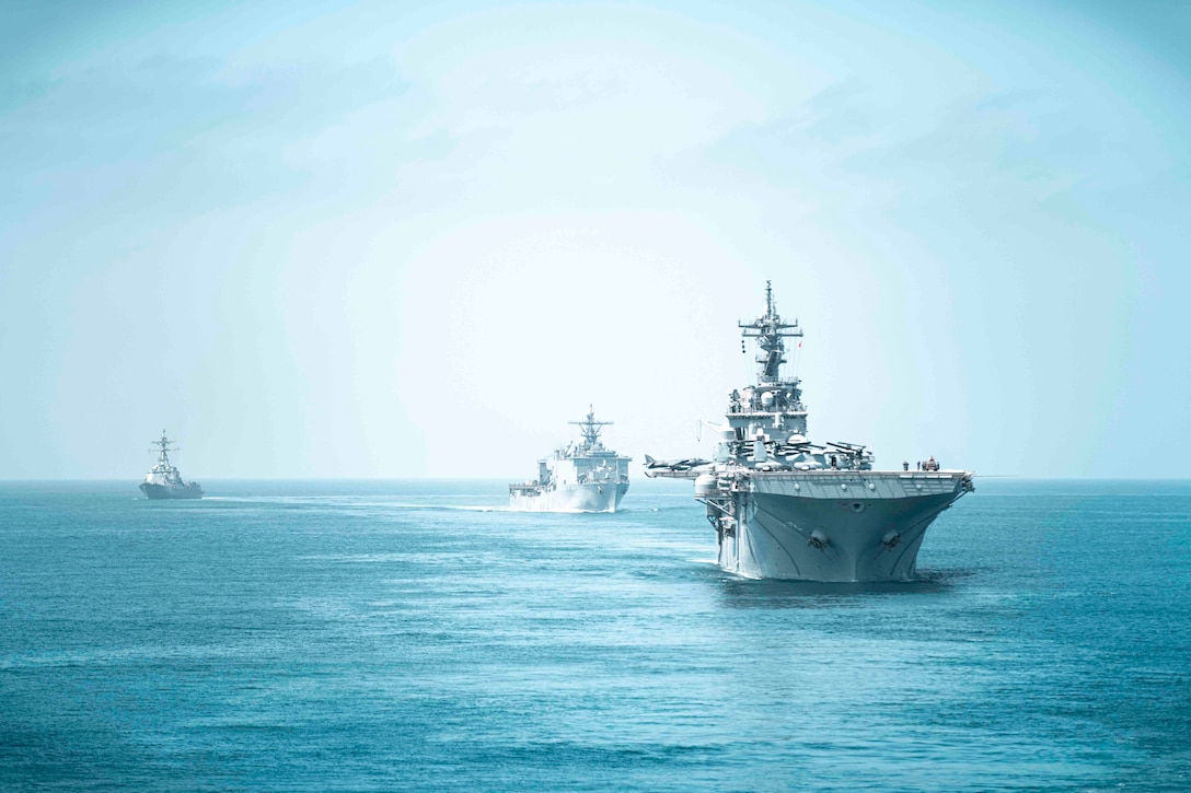 Three Navy ships sail in formation through waters.