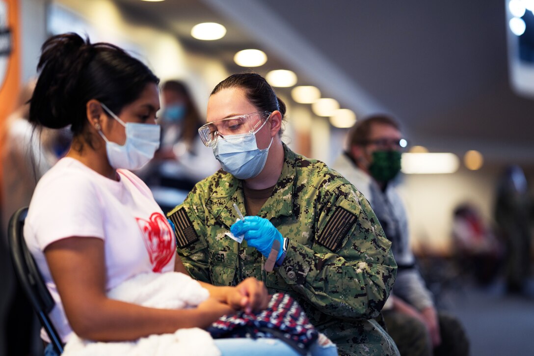 A sailor wearing a face mask and gloves kneels down to vaccine a resident.
