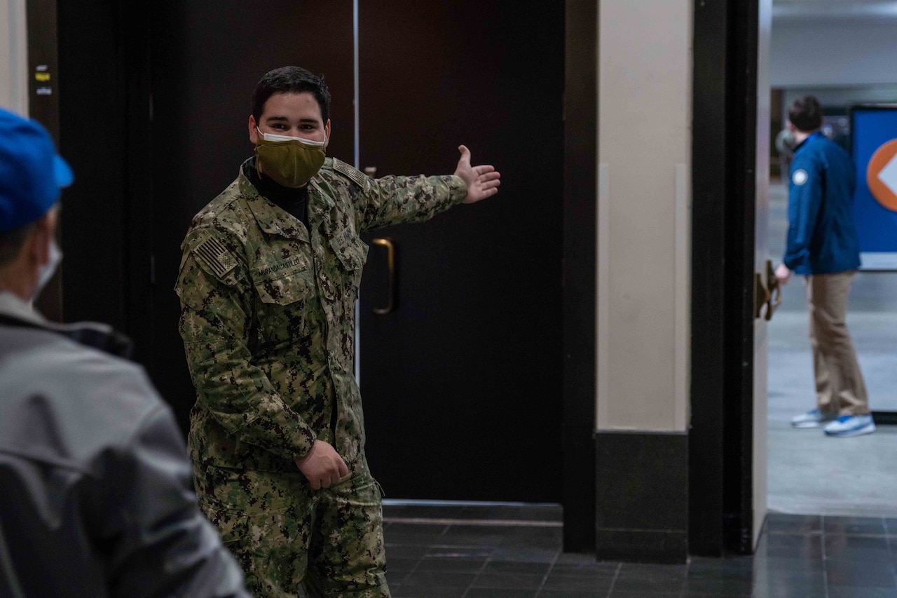 A sailor wearing a face mask guides patients to vaccination lines.