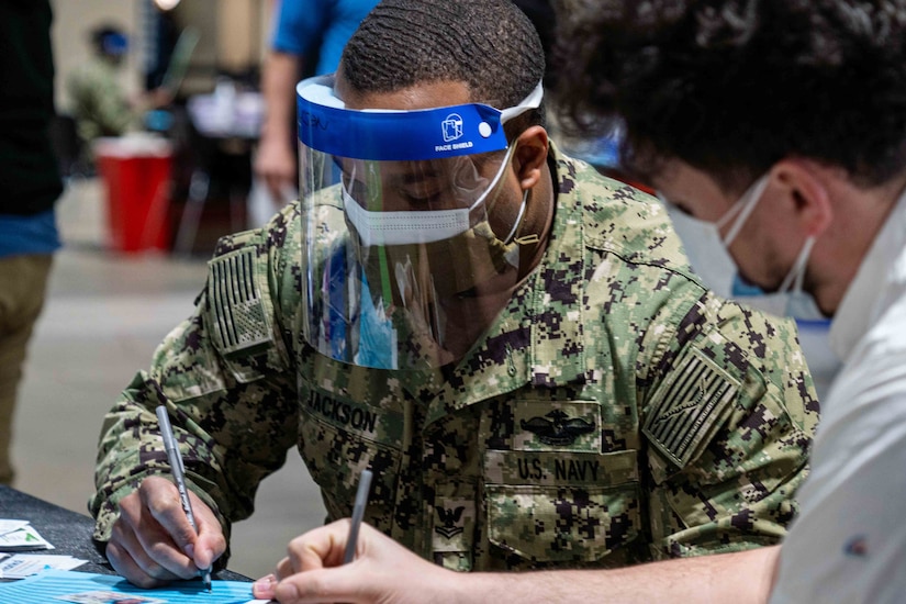 A sailor wearing a face mask documents info for a vaccine.
