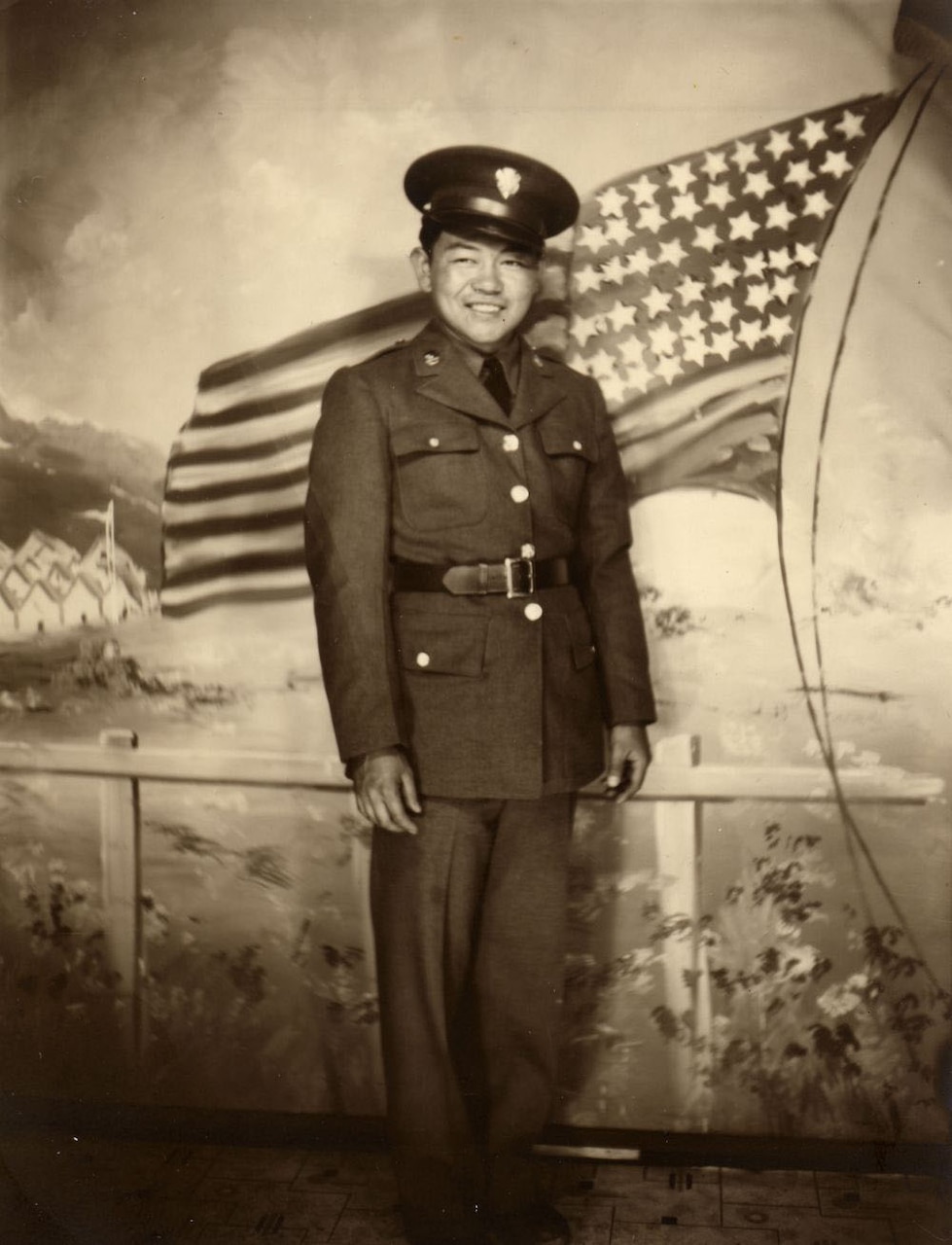 A man in uniform poses in front of a painting of a U.S. flag.