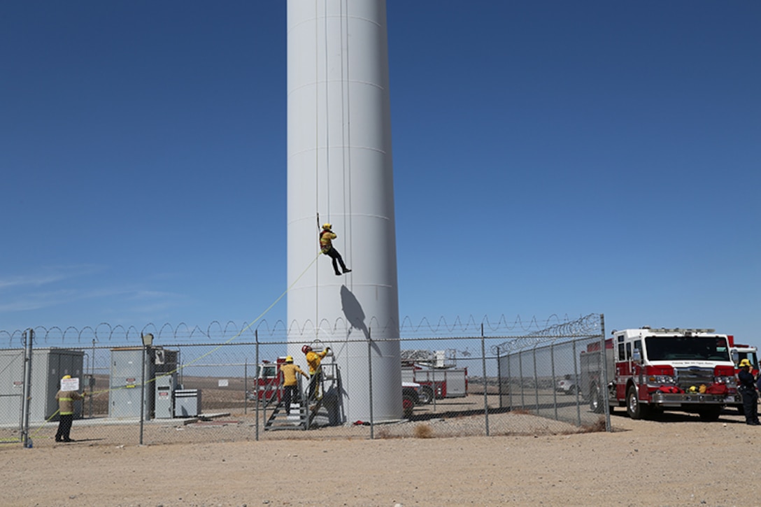 Eric Keck, firefighter/paramedic with Fire and Emergency Services, rappels 230 feet from a wind turbine as part of the Technical Rope Rescue training held aboard Marine Corps Logistics Base Barstow, California, April 15. Captain Tim Yonta, prepares to guide Keck safely to his feet once he reaches the platform below. The training was conducted by Tech Rescue Trainers, Inc. as part of a comprehensive series of technical rescue courses.
