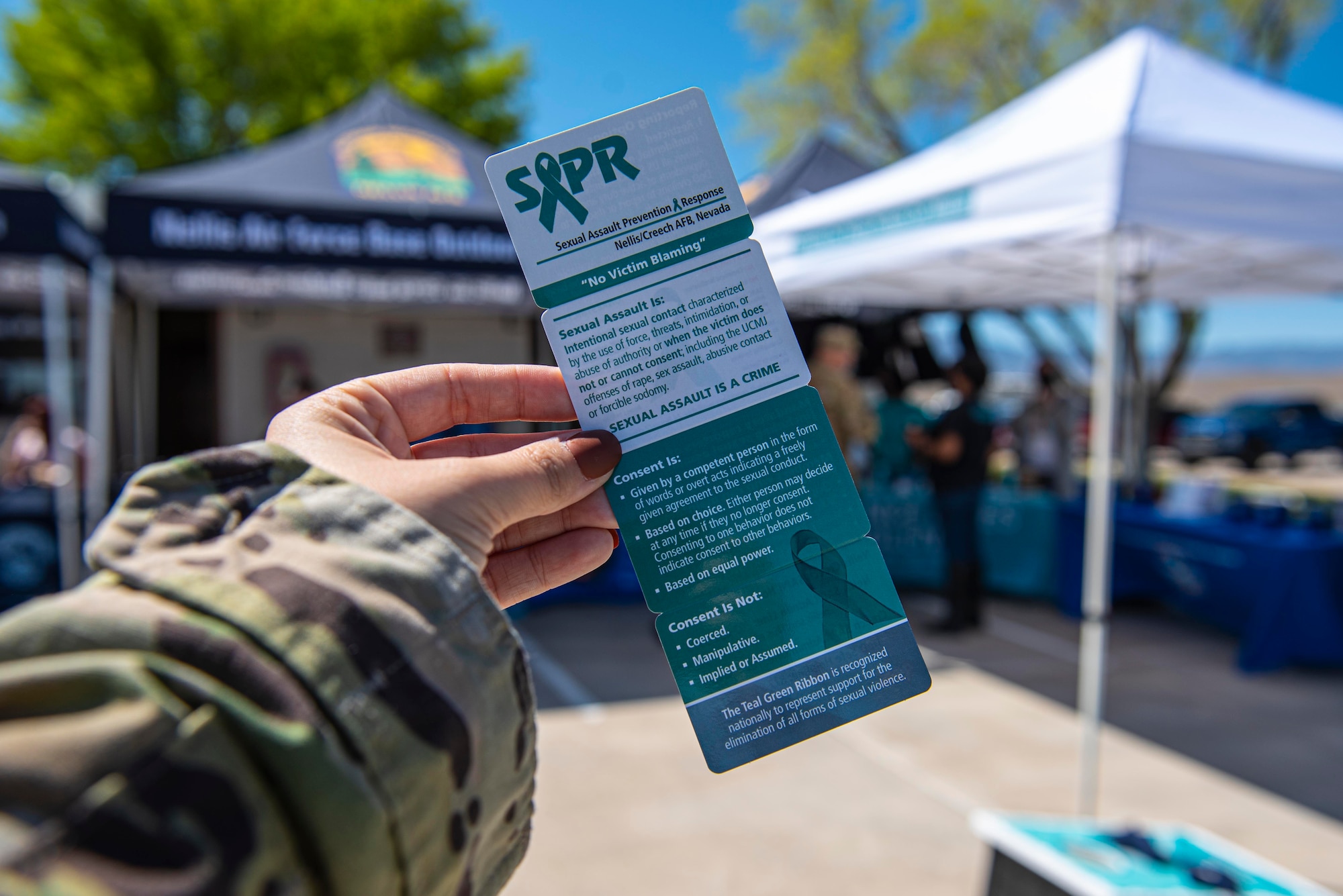 An Airman holds a Sexual Assault Prevention and Response information card in front of people attending a SAPR event.