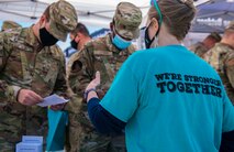 A woman's back is to the camera and the t-shirt reads "we're stronger together." The woman is talking to male Airmen who are reading a pamphlet.