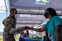 Woman in teal shirt hands male Airman a mask.