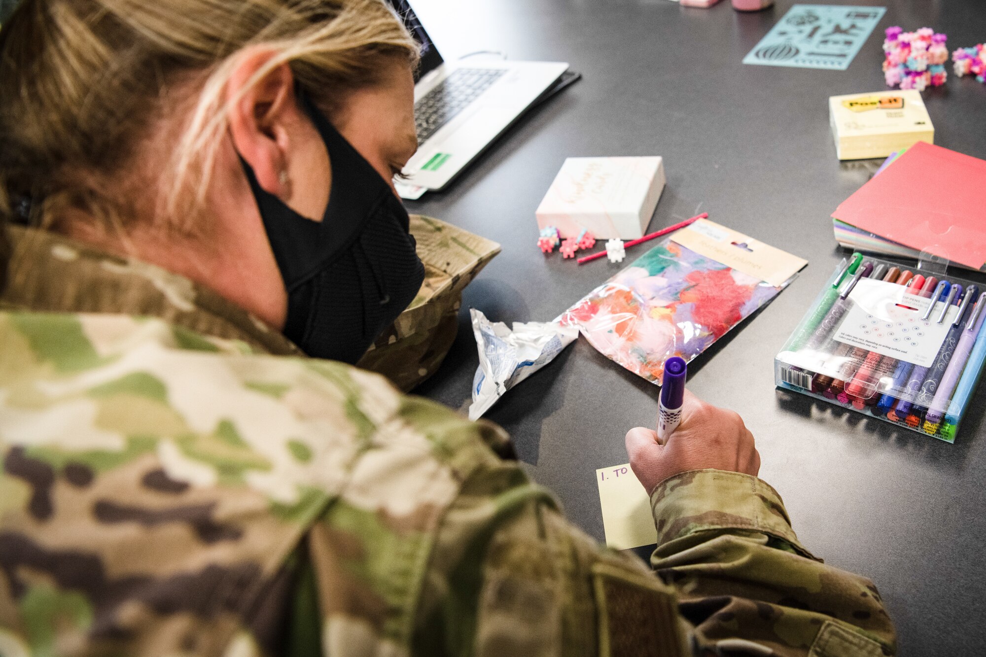 A female Airman writes on a sticky note with a purple marker.