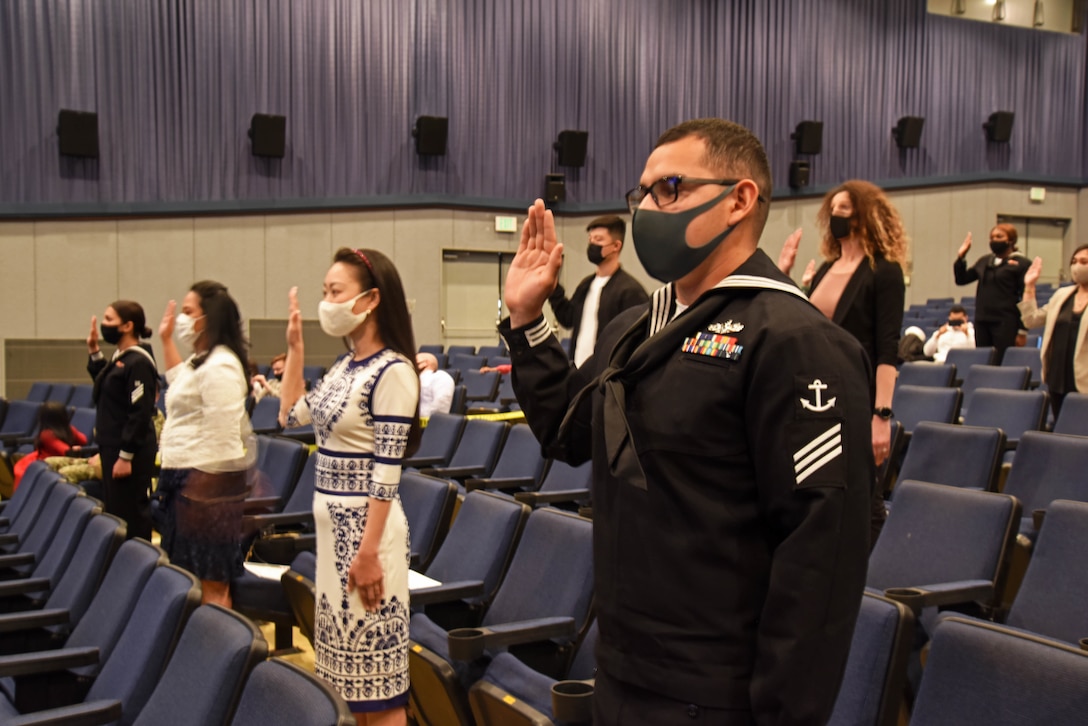 Seaman Armando Diaz-Mejia, right, civilians and fellow Sailors onboard Commander, Fleet Activities Yokosuka (CFAY) recite the Oath of Allegiance during a United States Citizenship and Immigration Services (USCIS) naturalization ceremony hosted by the Region Legal Service Office Western Pacific at Benny Decker Theater.