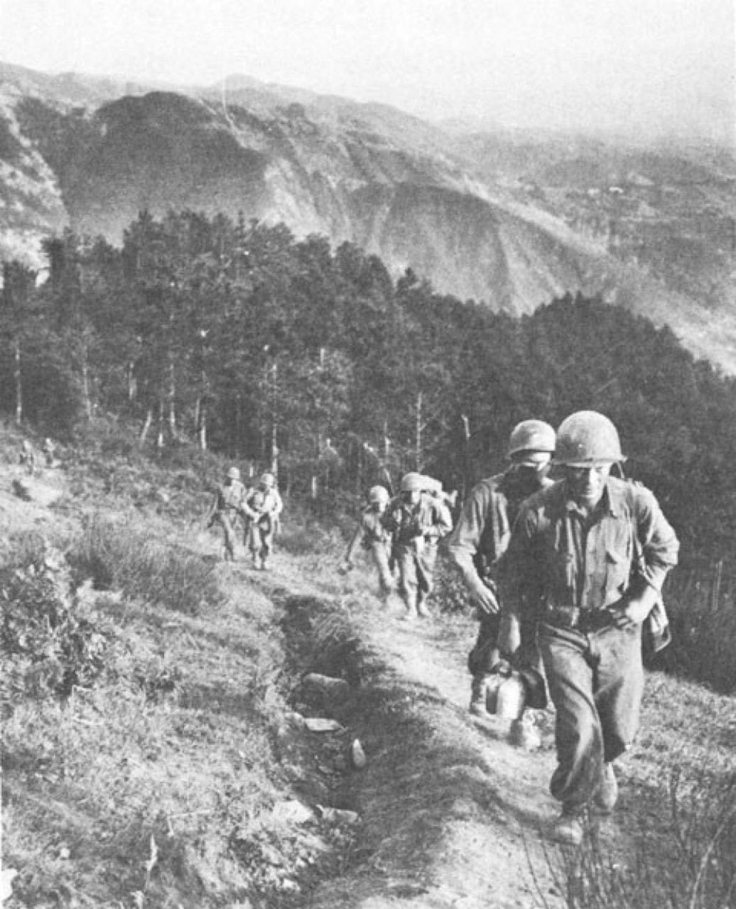 Soldiers march in line up a mountainside.