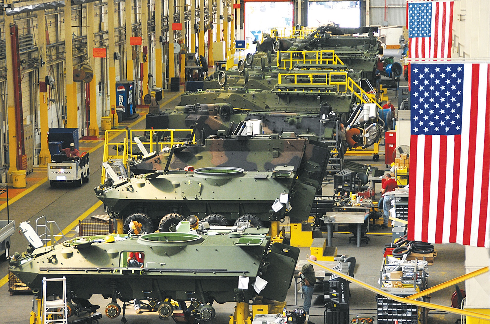 Large building at Marine Depot Maintenance Command, Barstow, California, shows mechanics performing maintenance on a variety of military vehicles.