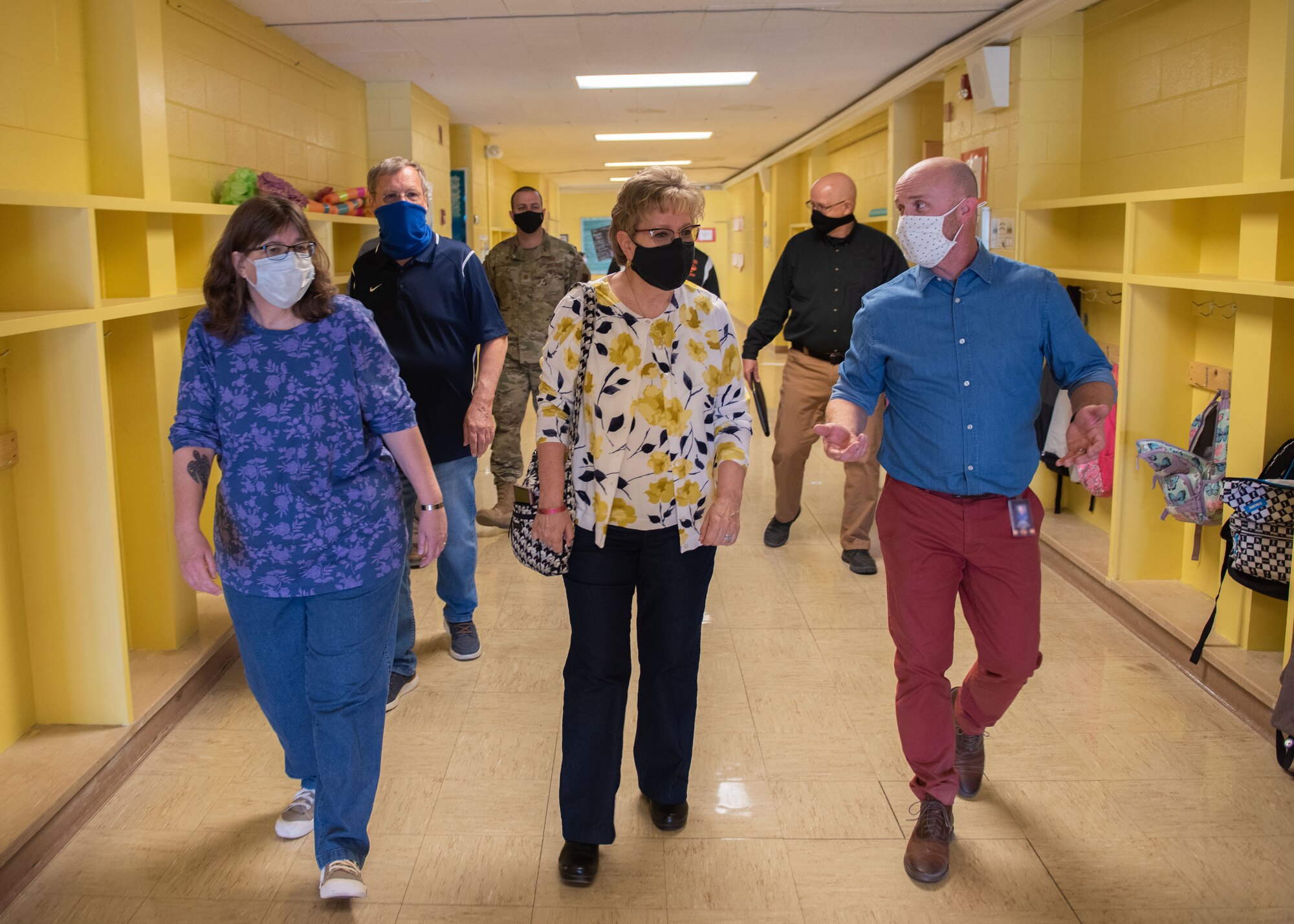 Seven individuals walk down a school hallway.