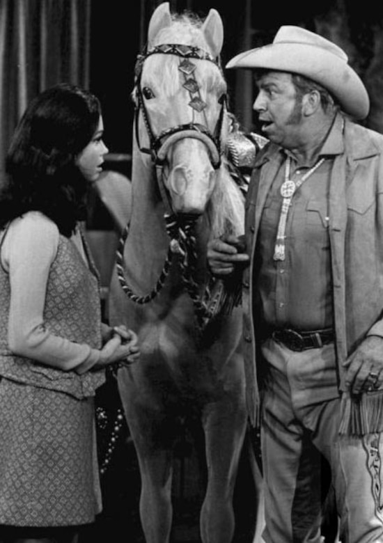 Actors talk on a Western set. There is a horse between them.