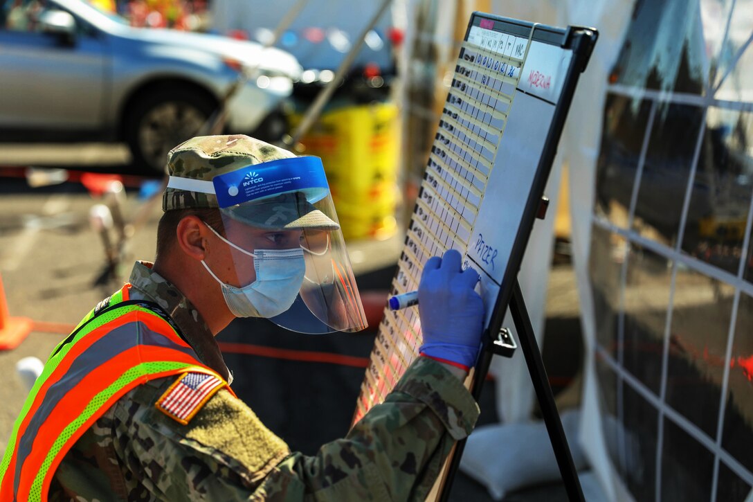 A soldier wearing a face mask and gloves writes on a board.